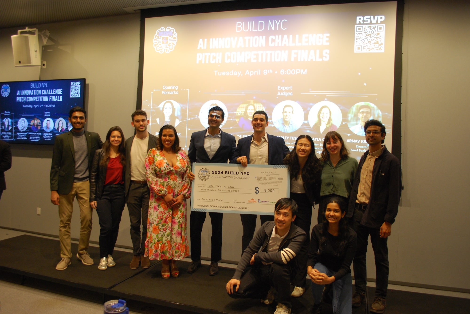 Impact Competition winners holding a large check in front of projector screen in classroom