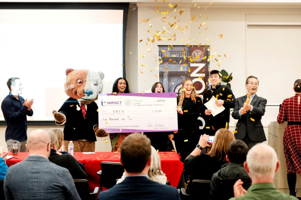 Three people holding a large check for $10,000 while an audience claps and confetti rains down